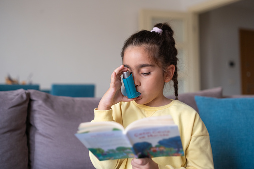 Una niña usa un inhalador para el asma mientras lee un libro en casa photo