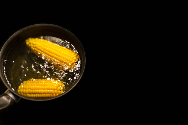 corn is boiling in a pan with hot water on a black background with space for text top view
