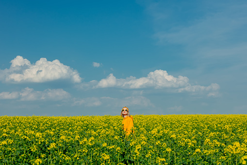 Stylish woman in yellow hoodie, cap and sunglasses in rapeseed field