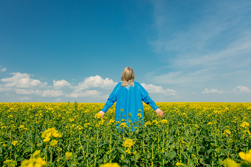 Stylish blond woman in blue shirt on blooming rapeseed field in spring