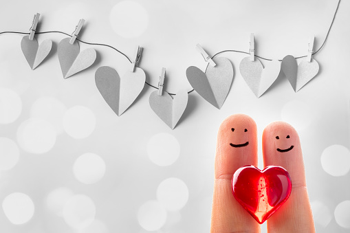 Funny finger couple with a red heart and paper cut hearts hanging on a clothesline with wooden clothespins. Beautiful defocused lights bokeh background. Space for copy.