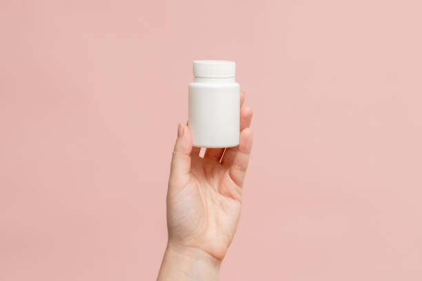 istock Plastic bottle (tube) in hand on pink background. Packaging for vitamins, tablets or capsule, or supplement 1779746890