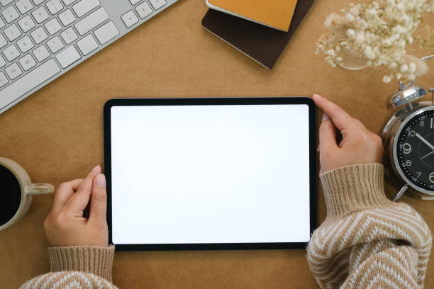 istock Woman hand holds digital tablet mockup with blank screen, education and application concept template, bright brow background, top view and copy space photo 1779765502