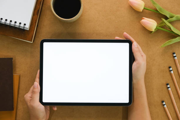 istock Woman hand holds digital tablet mockup with blank screen, education and application concept template, bright brow background, top view and copy space photo 1779765575