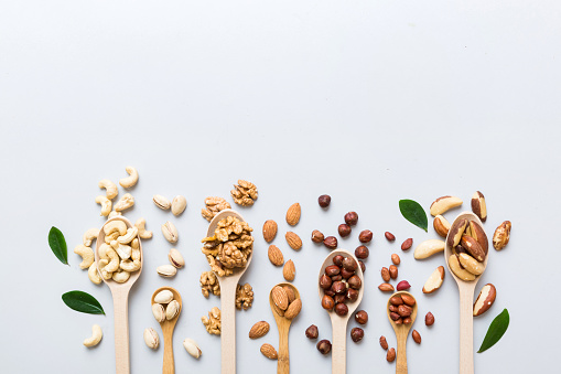 mixed nuts in white wooden spoon. Mix of various nuts on colored background. pistachios, cashews, walnuts, hazelnuts, peanuts and brazil nuts.