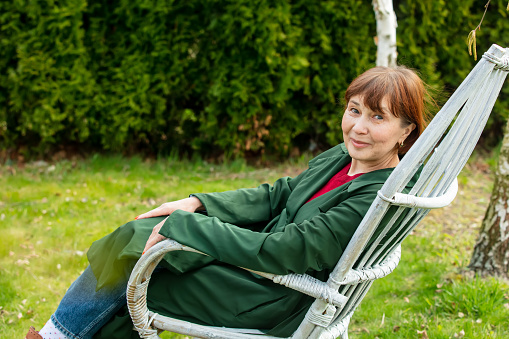 Senior woman sits in armchair in spring time garden