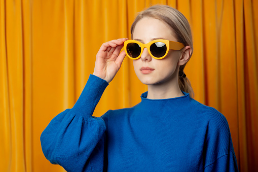 Stylish ukrainian woman in yellow sunglasses and blue sweater on curtains background
