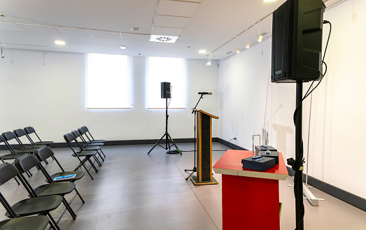 Modern and luminous room, empty, prepared for an event. Lectern with microphone and sound system and empty chairs to accommodate attendees