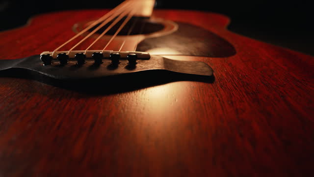 Slider macro of strings on redwood acoustic guitar fretboard. Music background.
