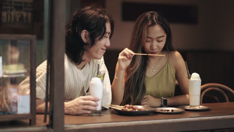 Happy young Asian couple dating in cafe, drinking chatting. Enjoying moment together