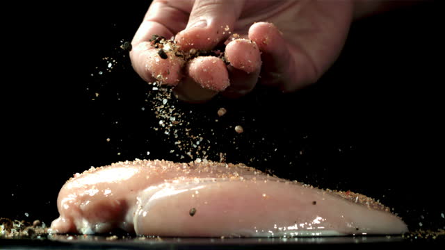 A man sprinkles spices on chicken fillet. Filmed on a high-speed camera at 1000 fps.