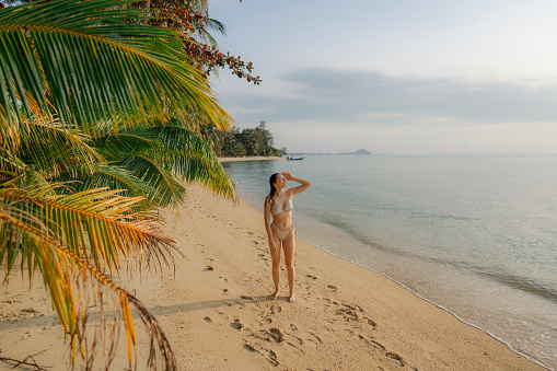 Young Caucasian woman in swimsuit walking  on the idyllic tropical beach