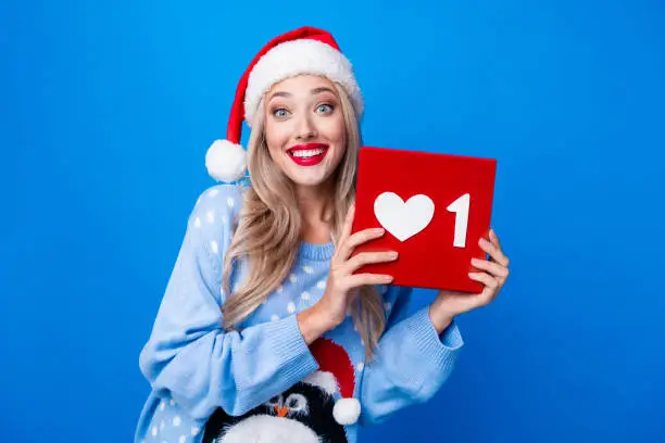 Photo of Photo portrait of attractive blonde woman hold notification like dressed penguin sweater x-mas hat isolated on blue color background