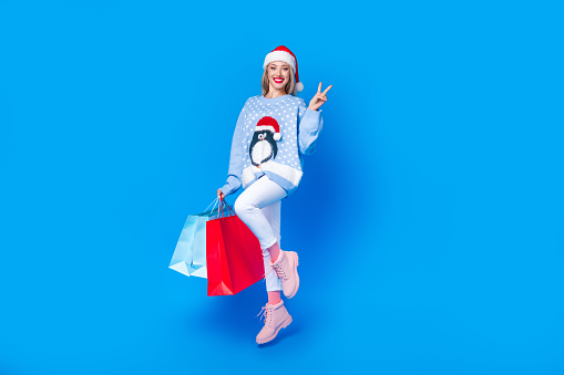 Full size body of friendly positive jump woman ready for shopping happy new year party show v sign isolated on blue color background.