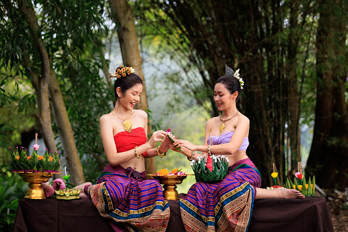 young woman in ancient thai dress helps each other to make krathong. in the nature background.
