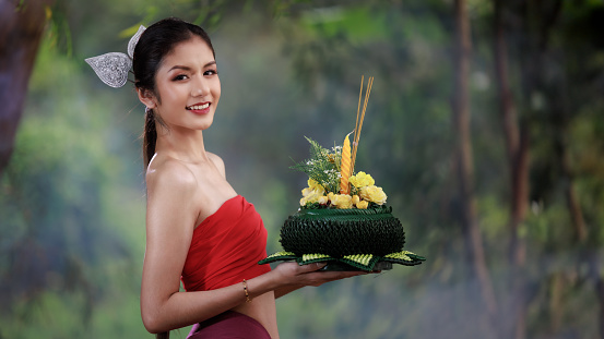 young woman in ancient thai red dress holding krathong on hands  in the nature background.