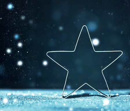 Sparkling Christmas Star on Dark Defocused Bokeh Background. Christmas Ornament on Glitter Defocused Blue Lights