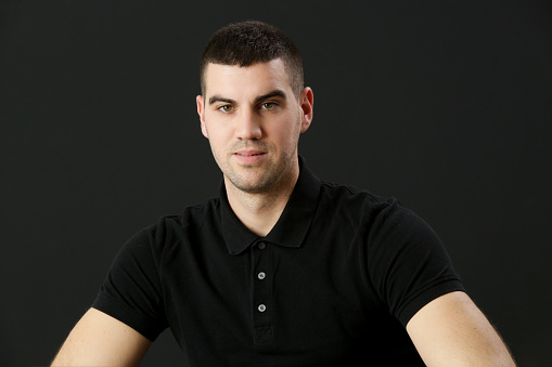 Studio portrait of young man in black polo shirt on the black background