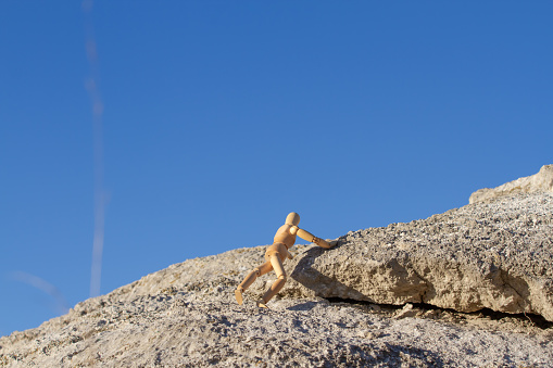Wooden figurine, mannequin climbing a bare rock. Concept of dealing with difficulties.