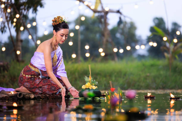 Loi Krathong Festival, Thai woman holding a krathong sitting on a raft by the river, Asian women in traditional Thai costumes bring krathongs to float on Loi Krathong Day, Loi Krathong Festival, Thai female holding a krathong sitting on a raft by the river, Asian women in traditional Thai costumes bring krathongs to float on Loi Krathong Day, loi krathong stock pictures, royalty-free photos & images