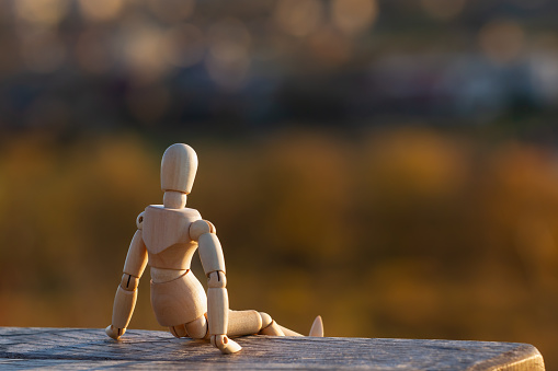 Wooden figurine of a man sitting with his back on a bench.