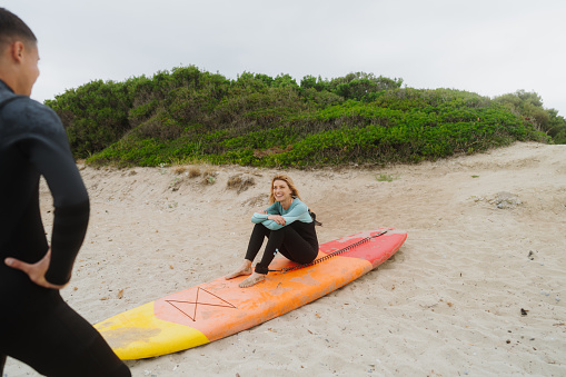 Photo of a couple of smiling people in wetsuits sitting on the beach, waiting for a good surfing waves