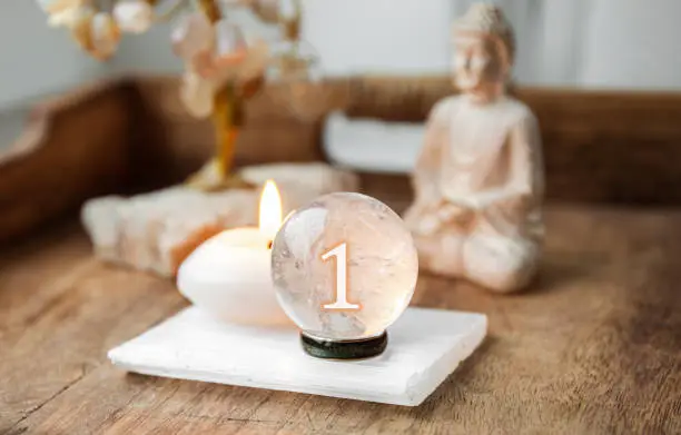 Number one on Gemstone sphere or crystal balls known as crystallum orbis and orbuculum. Natural clear quartz ball on stand on wood tray in home. Predictions concept.