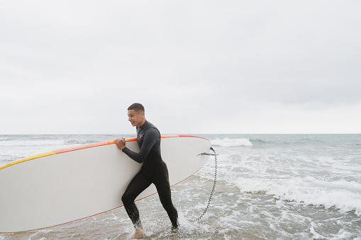 Photo of a teenage boy carrying his surfboard