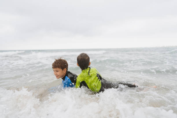 Photo is showing  two young boys in their wetsuits, enjoying their fulfilled summer vacation by the ocean
