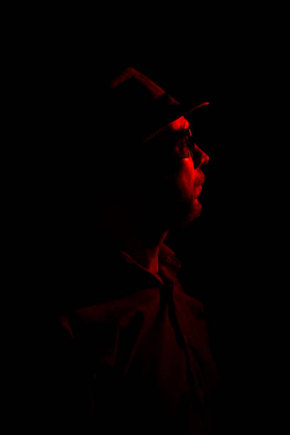 istock Man with hat on dark background, wearing sunglasses with red light on his face. 1779917709