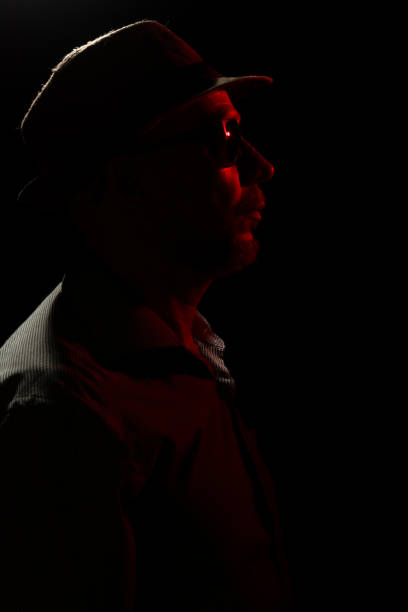 istock Man with hat on dark background, wearing sunglasses with red light on his face. 1779918264