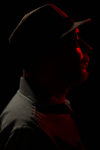 istock Man with hat on dark background, wearing sunglasses with red light on his face. 1779918786