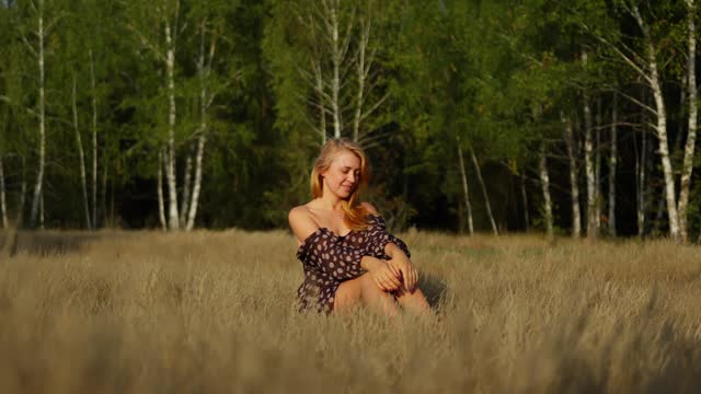 Beautiful young girl in a dot dress sits on an autumn field smiling and posing