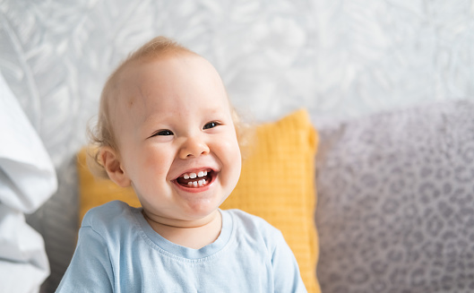 A close-up portrait of a funny little boy sitting on a bed and laughing