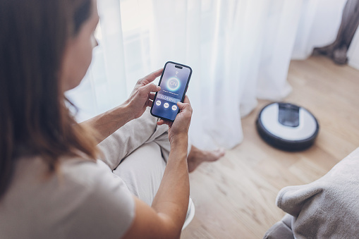 Woman using smart phone to control robot vacuum cleaner with an app