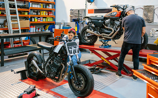 Mechanic couple team repairing custom motorcycles over platform on factory