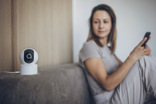 Woman using smart phone to control security camera at home