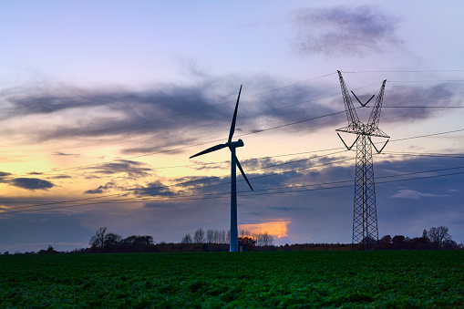 Wind turbine and pylon in agricultural field at dusk