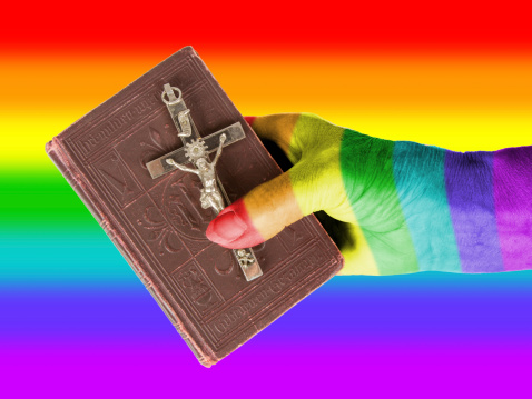 Hand (woman) holding a very old bible, rainbow flag
