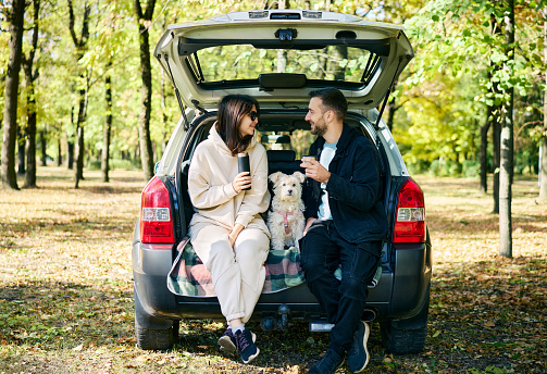 Couple with their dog relaxing in forest sitting in car trunk. Family, vacation, holidays, travel concept