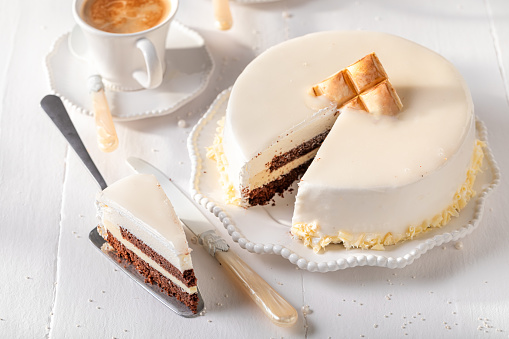 Delicious white chocolate cake served with coffee in white porcelain. White chocolate cake on white porcelain.