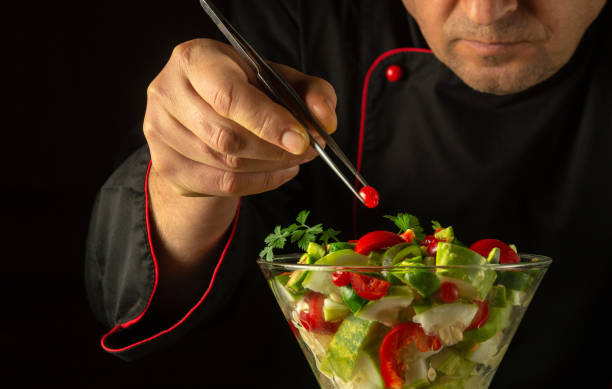 The cook prepares a salad with fresh vegetables and viburnum in the restaurant kitchen. Vegetable dish in a bowl for dinner. Vegetarian healthy food concept