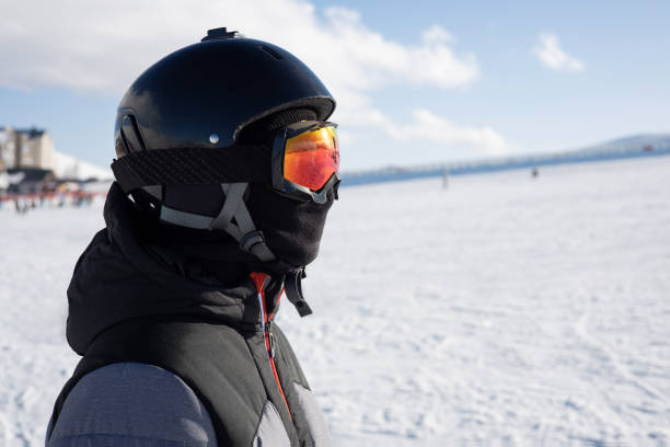 Girl or boy in ski helmet, sunscreen mask and balaclava close up stands against the backdrop of snow-covered mountain ski slope and a cloudy sky. Winter. Sport and travel content Girl or boy in ski helmet, sunscreen mask and balaclava close up stands against the backdrop of snow-covered mountain ski slope and a cloudy sky. snowboarding snowboard women snow stock pictures, royalty-free photos & images