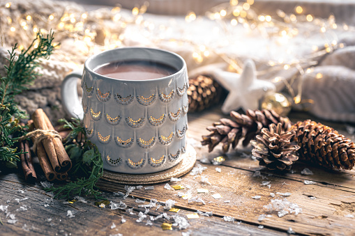 Coffee cup at home on a wooden table with bumps on a background with decorations, winter mood, holiday decoration, magic Christmas.