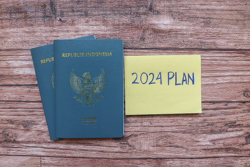 New year's resolutions 2024 on the table. Writing 2024 plan on sticky note with pen and passport on wood background. Passport and 2024 plan writing on wooden table. New Year 2024 Theme