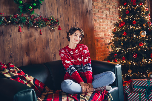 Photo of pretty young girl sit sofa netbook folded legs relax wear trendy red sweater festive interior living room presents christmas tree.