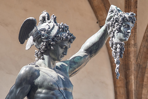 Close-up of Bronze statue of Perseus with the head of Medusa, a masterpiece by Benvenuto Cellini preserved in Florence, in the background the Loggia dei Lanzi in Florence
