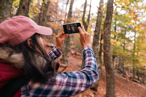 Young woman taking photos with mobile phone in autumn season