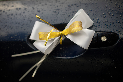 White bow on handle of car door. Rumbling transport to wedding. Bow made of fabric. Beautiful addition.