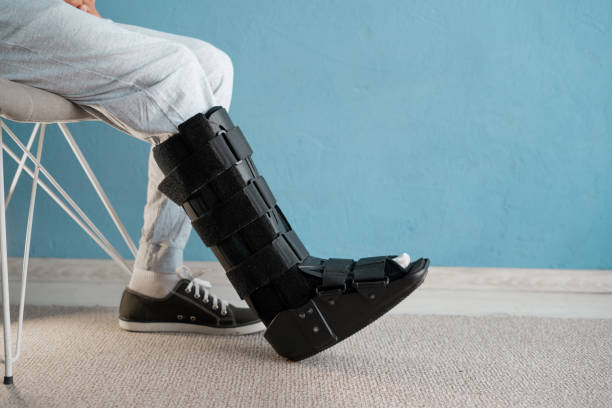 Injuried man with orthosis and sprained ankle sitting on the chair. Ankle orthosis concept Injuried man with orthosis and sprained ankle sitting on the chair. Ankle orthosis concept. Copy space Ankle Brace stock pictures, royalty-free photos & images